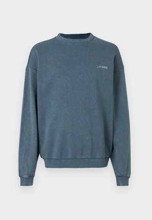 Bluza z długim rękawem i dekoltem typu crew neck w kolorze spranego niebieskiego, z prążkowanymi mankietami i dołem, z małym białym logo „ARKK” na lewej górnej części klatki piersiowej.