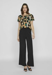 Blusa a stampa leopardo in tonalità di marrone e verde, abbinata a pantaloni larghi neri e décolleté aperti neri, creando una silhouette moderna.