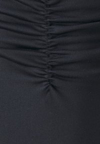 Svart, tettsittende stoff med samlet tekstur, med vertikale folder. Materialet ser elastisk og glatt ut.