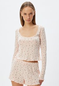 Ensemble de pyjama rose clair comprenant un haut à manches longues avec un col festonné et un motif floral, associé à un short assorti avec des bords ondulés.