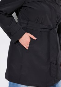 Czarny płaszcz trench z paskiem w talii, z guzicznymi mankietami i bocznymi kieszeniami, wykonany z gładkiego, trwałego materia łu.