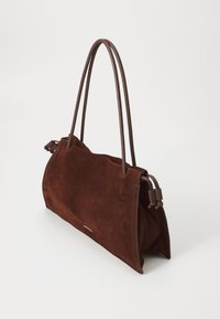 Geantă din suede maro, cu două mânere lungi din piele maro, o textură moale și un design spatios. Include accente cu franjuri și un logo subtil.