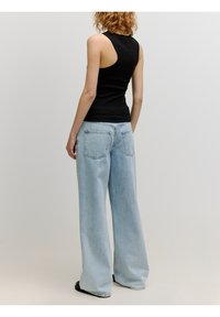Zwarte mouwloze top gecombineerd met lichtblauwe wijde jeans. De jeans hebben achterzakken en een relaxte pasvorm, gemaakt van denim stof.