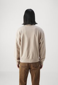 Beige sweatshirt med avslappnad passform, rund hals och ribbade ärmslut, ihop med bruna byxor. Mjuk textur med minimala designdetaljer.