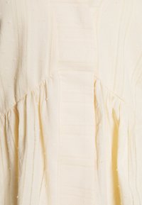 Vestito color crema chiaro con sottili bobble testurizzati, strisce verticali e vita arricciata per una silhouette fluida.