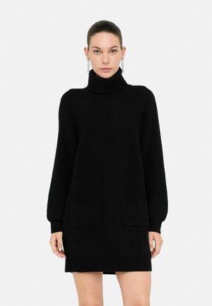 Abito a collo alto nero in maglia con maniche lunghe, caratterizzato da due tasche frontali e una vestibilità morbida. Materiale testurizzato con dettagli a coste.