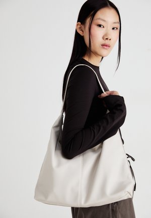 Beige håndveske laget av mykt materiale, med en slapp design, sydd detaljer og to skulderstropper. Passer for daglig bruk.