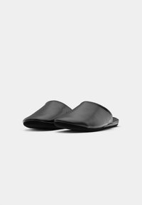 Par de chinelos de couro preto, em estilo slip-on, com pontas quadradas arredondadas, em uma superfície lisa de tom cinza claro.