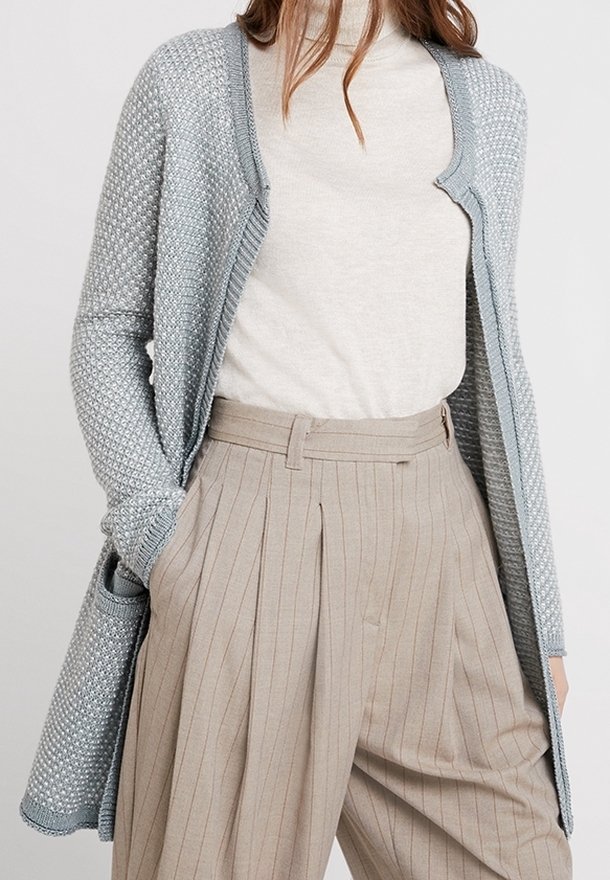 Ljusblå öppenstickad kofta med en texturerad yta, kombinerad med en beige höghalserad tröja och smalrandiga byxor med veck och hög midja.