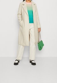 Beige vlněný kabát, modro-růžový pruhovaný svetr, krémové kalhoty, černé a stříbrné boty a zelená pletená kabelka.