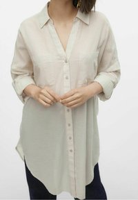 Camicia a righe di colore chiaro, con colletto, due tasche sul petto e maniche arrotolate. Realizzata in un tessuto morbido e strutturato.