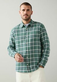 Green and white plaid flannel shirt with long sleeves, button-down front, and soft texture, paired with light-colored pants.