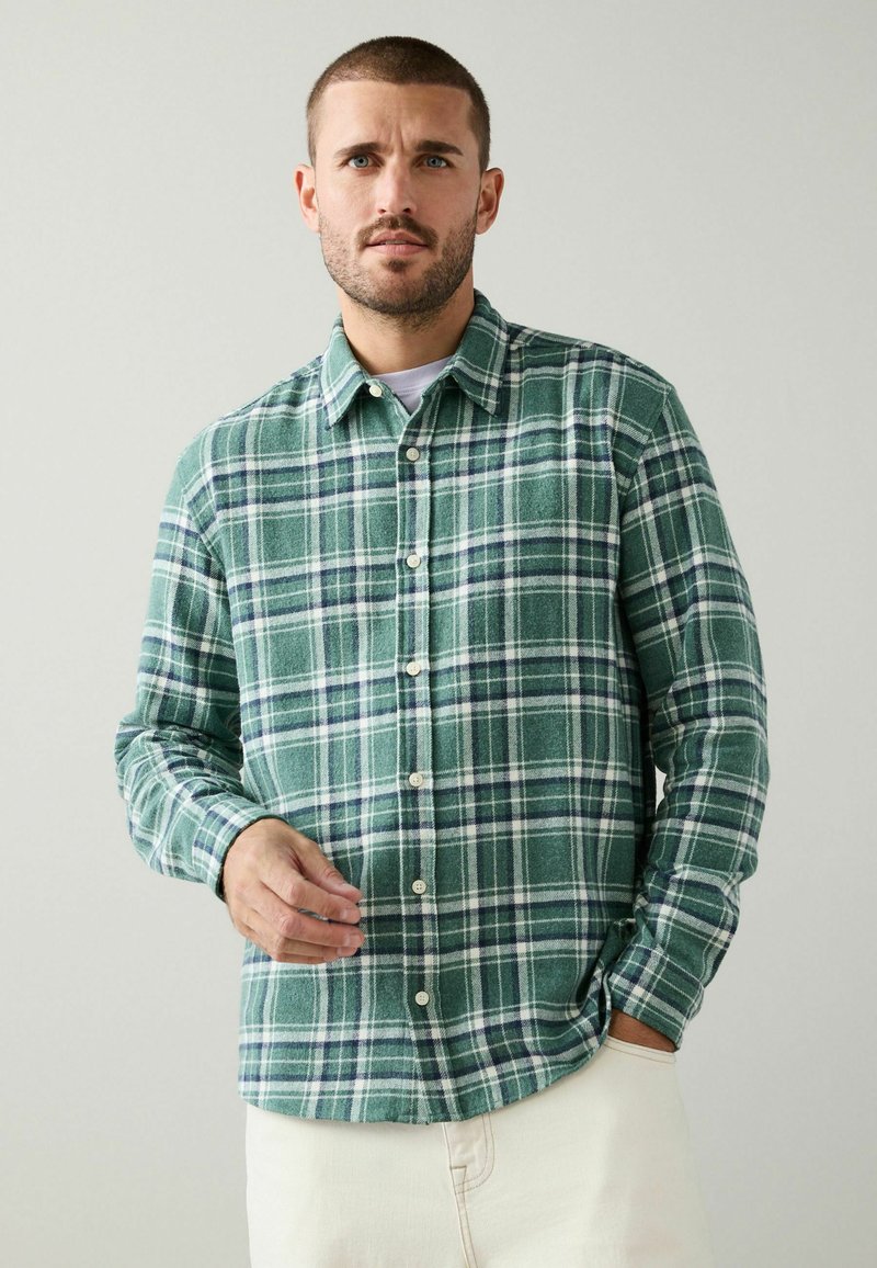 Green and white plaid flannel shirt with long sleeves, button-down front, and soft texture, paired with light-colored pants.
