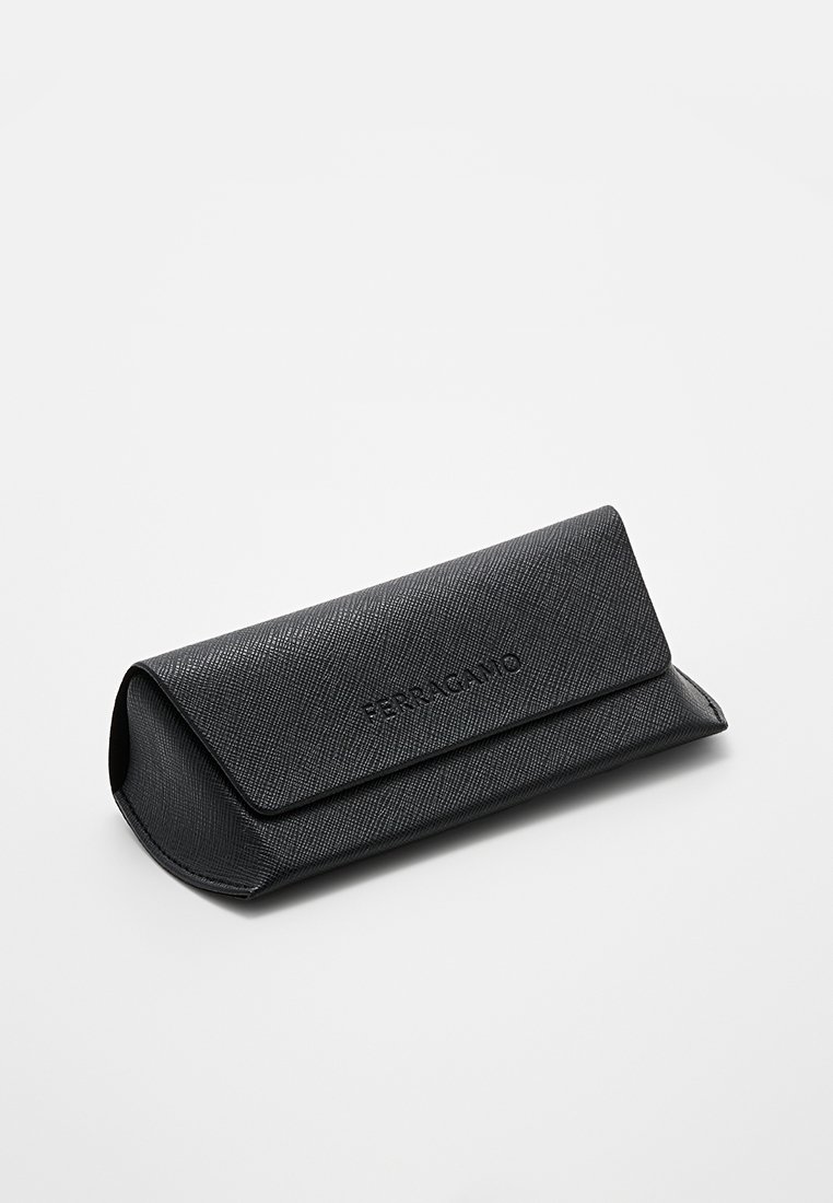 Étui pour lunettes en cuir noir texturé avec un rabat arrondi et un logo en relief. Design compact, présentant une finition lisse et un léger brillant.