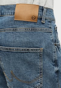 Κοντινό πλάνο πίσω τσέπης μπλε τζιν με καφέ δερμάτινο σημείο και διακριτικό ραμμένο σχέδιο στην τσέπη.