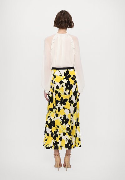 White blouse with ruffled back detail, paired with a long yellow skirt featuring a bold black and white floral pattern. Transparent fabric.