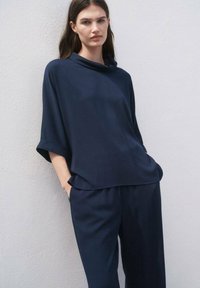 Top azul marino de corte oversized con cuello de drapeado y mangas cortas, combinado con pantalones sueltos azul marino. Tejido suave con una textura sutil.