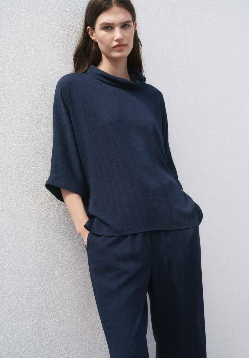 Top azul marino de corte oversized con cuello de drapeado y mangas cortas, combinado con pantalones sueltos azul marino. Tejido suave con una textura sutil.