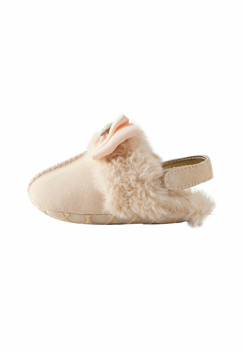 Chaussure bébé beige douce avec une doublure duveteuse, une bride arrière et un nœud rose sur le dessus, vue de côté sur fond blanc.