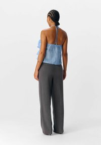 Top halter blu textured con dettagli arricciati, abbinato a pantaloni grigi lunghi e su misura, visto da dietro su uno sfondo bianco.