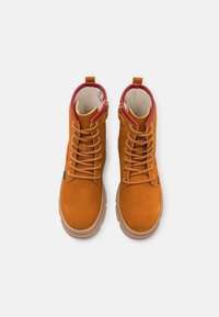 Brown suede ankle boots with red textile lining, rounded toe, and tan rubber sole; features laces and a side zipper for easy wear.