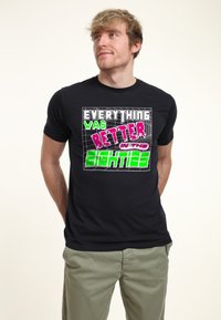 Camiseta de algodón negra con un gráfico en el que aparece un texto retro en rosa, verde y blanco que dice "Todo era mejor en los ochenta".