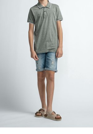 Grijze polo met witte kraag en bies, gecombineerd met opgerolde denim shorts. Beigekleurige sandalen met een strikaccent en kurkzool.
