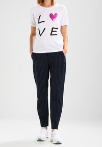 Camiseta de algodón blanca con letras negras que dicen "LOVE" y un corazón rosa. Pantalones de rayas navy y zapatillas deportivas blancas.