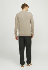 Pull en tricot marron clair avec un col rond, des manches longues et un ourlet côtelé, associé à un pantalon noir et des chaussures beige.