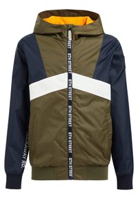 Olivově zelená větrovka s námořnickými modrými akcenty, bílým pruhem, kapucí a oranžovým podšíváním. Obsahuje zip a žebrované manžety.