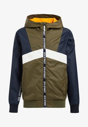 Vindjakke i olivengrøn med marineblå accenter, hvide striber, hætte og orange foring. Har lynlås og ribbede manchetter.