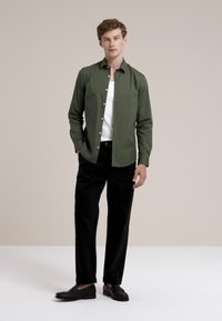 Camisa de botón verde olivo con mangas largas, camiseta interior blanca, pantalones negros y mocasines negros. Diseño simple, sin patrones visibles.
