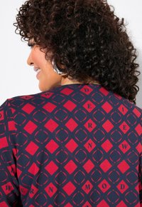 Tessuto a fantasia rosso e blu navy con forme geometriche a rombo e testo stilizzato. Texture morbida e aspetto leggero.