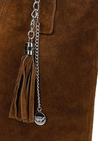 Borsa in suede marrone con catena argentata, dettaglio con nappina e charm metallico brandizzato. Texture liscia con una sottile profondità e dettaglio.
