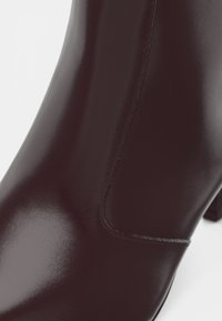 Detailný záber na lesklú čiernu koženú členkovú bootu s viditeľným šitím a blokovým opätkom.