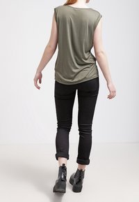 Top corto verde oliva a maniche corte con una vestibilità rilassata, abbinato a jeans skinny neri con risvolto e stivaletti neri.