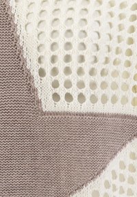 Primo piano di tessuto lavorato a maglia beige e bianco con fori a forma di diamante aperti e sezioni a trama solida.