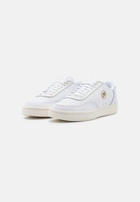 Vita sneakers i läder med ett perforerat mönster på sidorna, vita snören och en beige gummisula. Guld-logotyp på sidan.