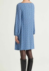 Robe à motifs bleus avec manches longues bouffantes, silhouette droite et encolure bateau, associée à des bottes noires brillantes montant jusqu'aux genoux.