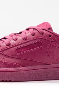 Gros plan sur une sneaker Reebok magenta montrant le logo en relief, les lacets en tissu, les coutures détaillées et la semelle texturée sur fond blanc.