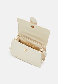 Beżowa torebka wykonana z gładkiego materiału, z złotym zapięciem i jednym paskiem. Wnętrze z widoczną kieszenią i miękką podszewką.