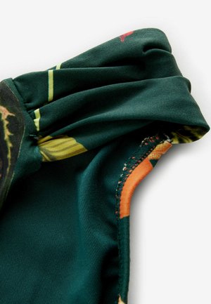 Grüner Stoff mit floralem Muster, versehen mit gefältelten Details und einem orangefarbenen Akzent. Glatte Textur mit einem genähten Rand.