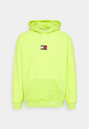Jasno żółto-zielona bluza z kapturem z przednią kieszenią, sznurkami i małą naszywką z logo Tommy Jeans na środku klatki piersiowej.