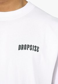 Hvid bomulds t-shirt med en sort grafisk tekst "DROPSIZE" i en fed, vinkelret skrifttype på venstre brystområde. Glat tekstur, klassisk pasform.