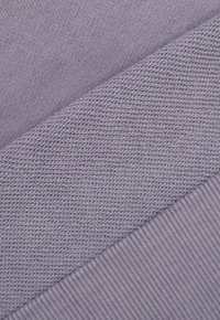 Fioletowa dziana tkanina z teksturowanym wzorem ściegów oraz gładką sekcją ściągacza, prezentująca różnorodność w stylu i wykończeniu dzianiny.