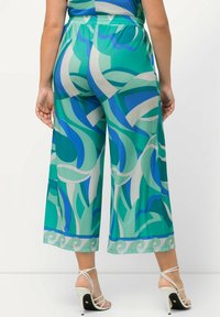Pantalons évasés en turquoise et vert avec des motifs abstraits de vagues. Fabriqués dans un tissu lisse, ils présentent une coupe décontractée et une taille élastique.
