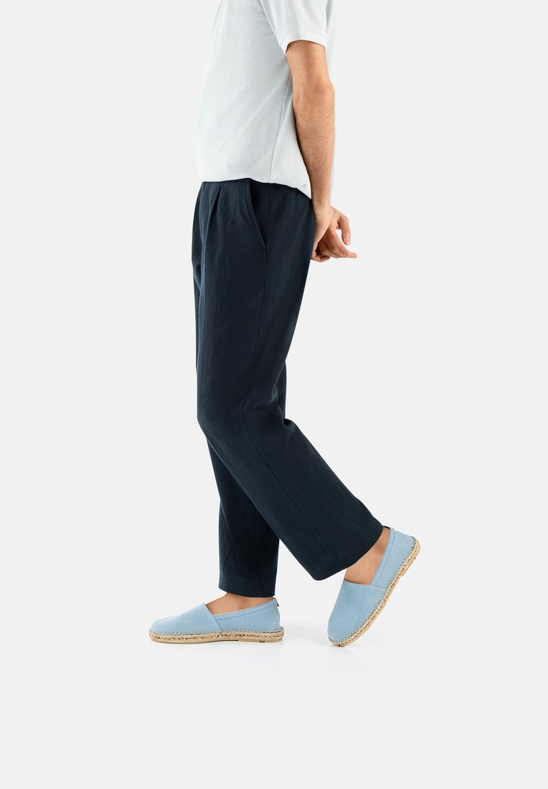Lichtblauwe espadrilles met juten zolen, gedragen met donkere, losse broeken. De stof lijkt zacht met een gladde textuur.
