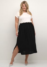 Sort maxi nederdel med elastisk talje og sidelæg, parret med en hvid t-shirt med korte ærmer og sølvfarvede spidse hæle.