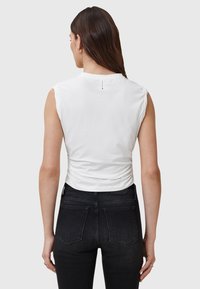 Top bianco senza maniche con design arricciato sul retro; tessuto liscio; abbinato a jeans neri a vita alta con tasche posteriori.