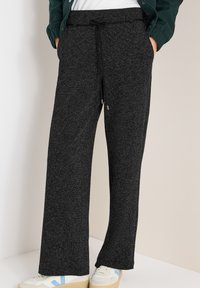 Pantaloni della tuta neri e strutturati con coulisse in vita, caratterizzati da una vestibilità comoda e tasche laterali. Abbinati a sneakers di colore chiaro.